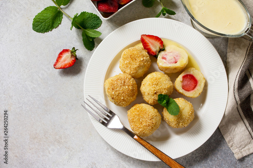 Cottage cheese dumplings with fresh strawberry, served with sour-honey sauce, delicious summer dessert on a bright stone table. Top view flat lay background, copy space.