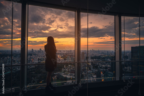 Rear view of Traveler woman looking Tokyo Skyline and view of skyscrapers on the observation deck at sunset in Japan. © nuttawutnuy