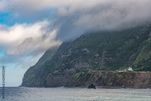 A spectacular coastline with cliffs and low cloud. A white church can be seen on a plateau by the cliffs. Taken on the west coast of the island of Flores in the Azores. 