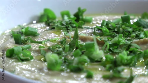 Hummus fresh with greens in a ceramic plate close-up.