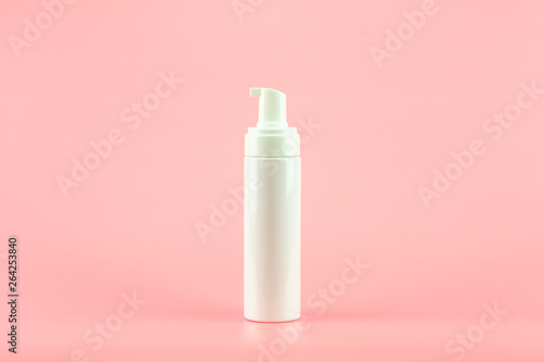 White plastic cosmetic lotion bottle on pink background.