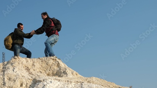 two climbers climb one after another on white rock. teamwork of business people. tourists give hand to each other, climbing to top of hill. team of male travelers goes to victory and success.