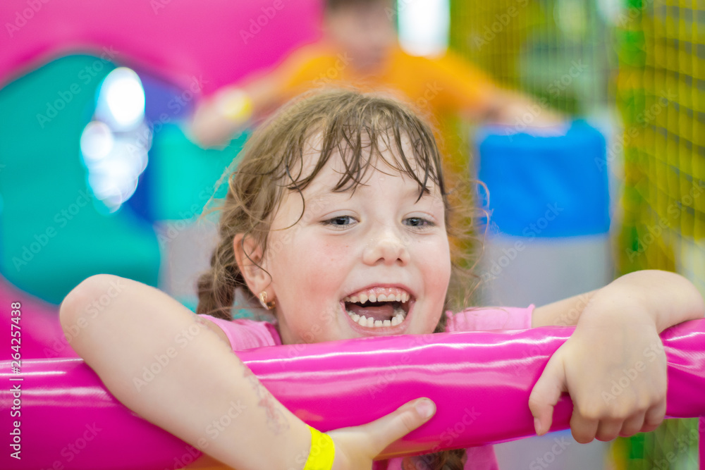 Portrait of a small beautiful girl in the play area of a children's entertainment center. A happy child pulls himself up on a soft colorful bar. Baby laughs enthusiastically. Portrait of a small beautiful girl in the play area of a children's entertainment center. A happy child pulls himself up on a soft colorful bar. Baby laughs enthusiastically.