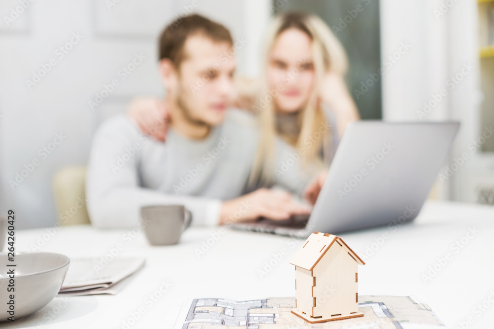 Lovely young couple, using a laptop and choosing a new apartment. Layout of the house in the foreground. Lovely young couple, using a laptop and choosing a new apartment. Layout of the house in the foreground.