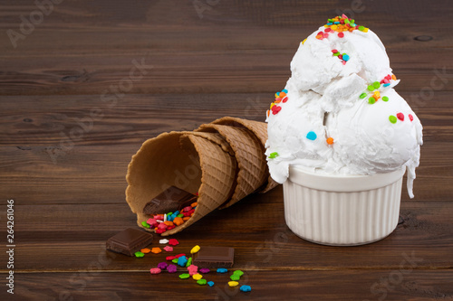 plate of vanilla ice cream scoop swith sprinkles and waffle cones on wooden background with copy space