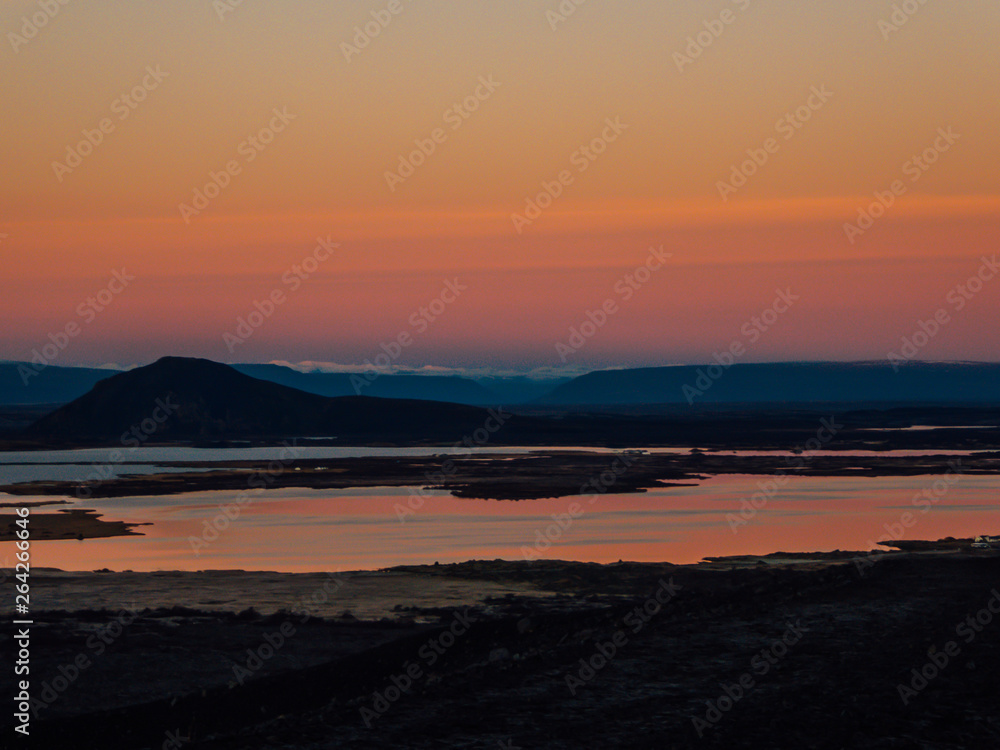 Pinkish sunset over a lake and mountains seen from a top of a volcano. Colors of the sky reflect in the water. Soft landscape. New day is born. Beauty of the nature. White mountain peaks in the back