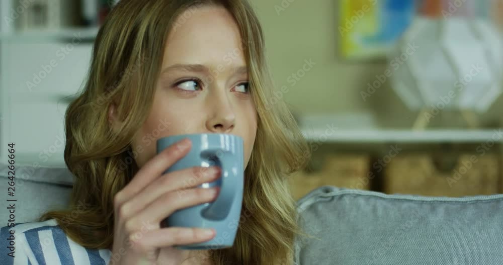 Close up of the good looking Caucasian young woman drinking tea or coffe while resting on the sofa at home. Close up of the good looking Caucasian young woman drinking tea or coffe while resting on the sofa at home.