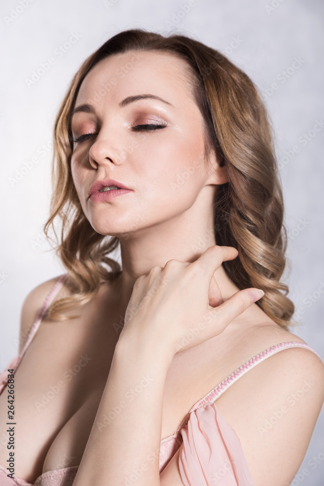 Fototapeta premium Portrait of beautiful young elegant female in pale pink wedding dress with big neckline, on a white background.