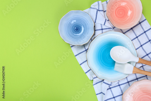 Various kitchen utensils, plates and a towel on a green background. Top view.