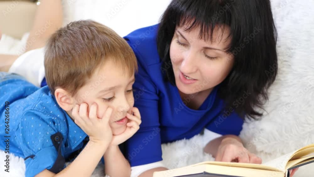 Happy mother reading a book to her child on a white sofa Happy mother reading a book to her child on a white sofa