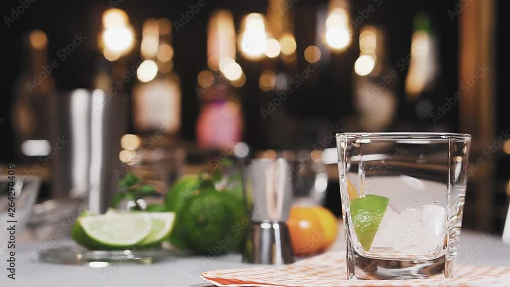 Bartender puts a piece of lime and pours liquor from jigger into glass and make a cocktail, slow motion. Cocktails with mint and lime. Bartender puts a piece of lime and pours liquor from jigger into glass and make a cocktail, slow motion. Cocktails with mint and lime.