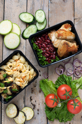 ready cooked meal to eat in lunch boxes, raw vegetables around, food containers on wooden table