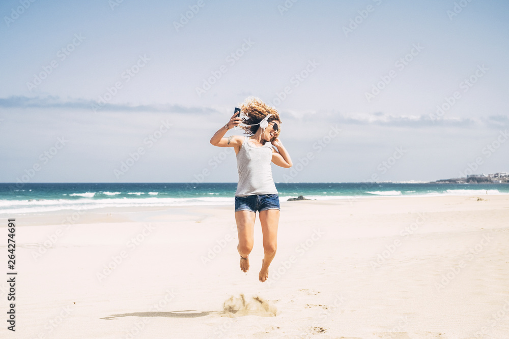 Happiness and joyful people concept with young beautiful curly caucasian woman jumping like crazy at the beach during summer holiday vacation leisure activity - headphones and mobile phone Happiness and joyful people concept with young beautiful curly caucasian woman jumping like crazy at the beach during summer holiday vacation leisure activity - headphones and mobile phone