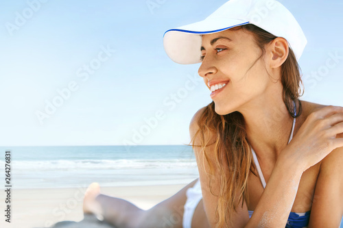 close up view of beautiful athletic woman tanning in bikini and white cap on sandy beach at summer. Model is relaxing lying down on white sand tropical getaway. Summer vacation concept.