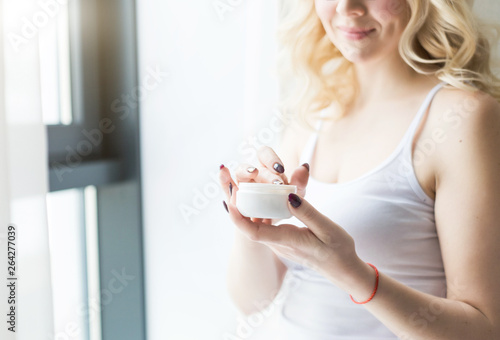 A beautiful blonde woman holds a jar of cream in her hand and applies it to her body. Skin care by moisturizing