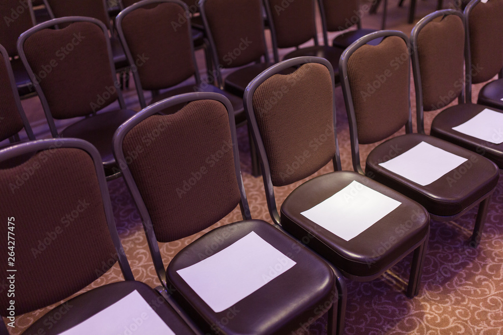 Obraz premium Brown chairs the conference hall before the event. First row for special guests. Empty places for your inscriptions on white paper sheets.