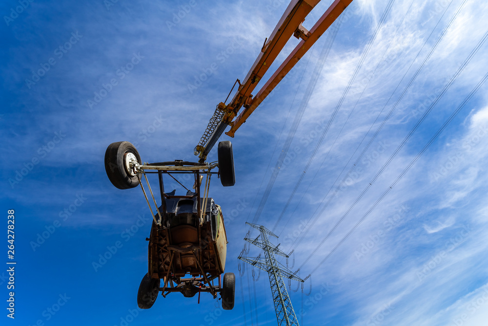 The frame of an old car is suspended on the boom of a crane on a background of blue sky. The frame of an old car is suspended on the boom of a crane on a background of blue sky.
