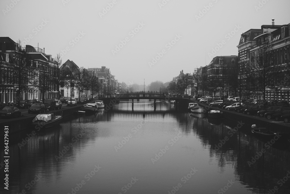 Charming cityscape of old Dutch town Haarlem. Stone bridge connecting two banks of the Spaarne river. Beautiful perspective. Misty and cloudy early spring weather. Black and white