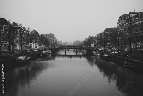 Charming cityscape of old Dutch town Haarlem. Stone bridge connecting two banks of the Spaarne river. Beautiful perspective. Misty and cloudy early spring weather. Black and white