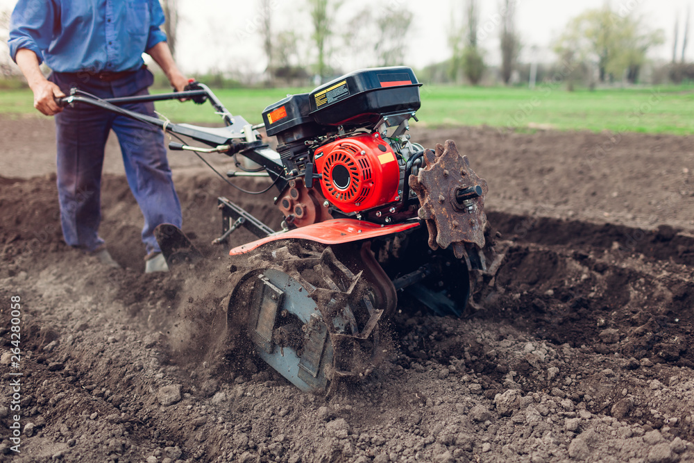 Farmer driving small tractor for soil cultivation and potato planting. Spring preparation Farmer driving small tractor for soil cultivation and potato planting. Spring preparation