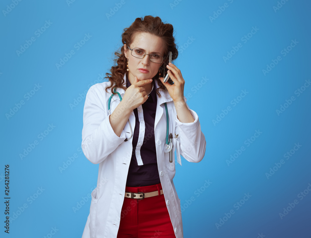 pensive medical doctor woman speaking on mobile phone on blue pensive medical doctor woman speaking on mobile phone on blue