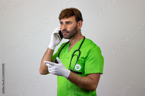 Portrait of male veterinary doctor in green uniform with brown hair speaking on the phone, facing forwards and looking at the horizon. Isolated on white background.