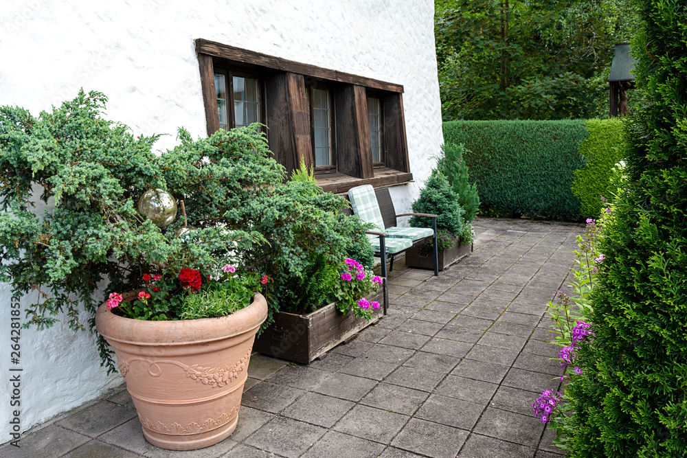 The territory of the house is decorated with a huge ceramic pot with flowers and coniferous trees.
