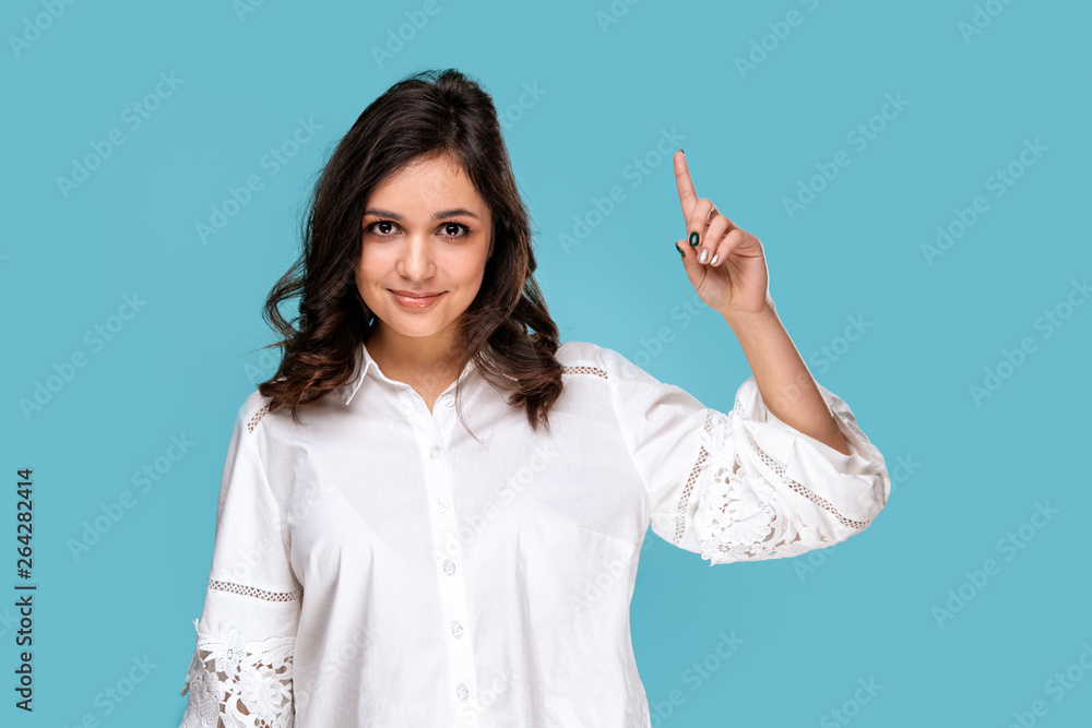 Pretty brunette girl pointing something by finger isolated over the blue background Pretty brunette girl pointing something by finger isolated over the blue background