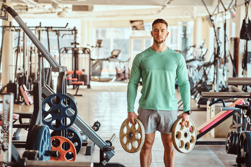 Sportive attractive man in green training shirt is doing his exsercises in gym with weights. photo