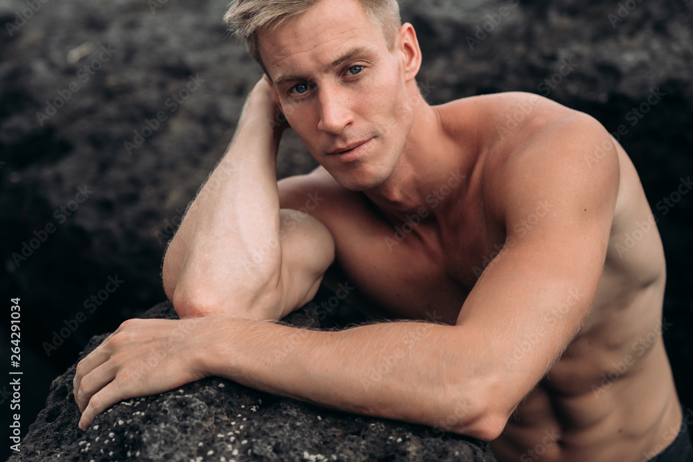 Portrait of sexy guy with bare-chested rests on beach with black sand Portrait of sexy guy with bare-chested rests on beach with black sand