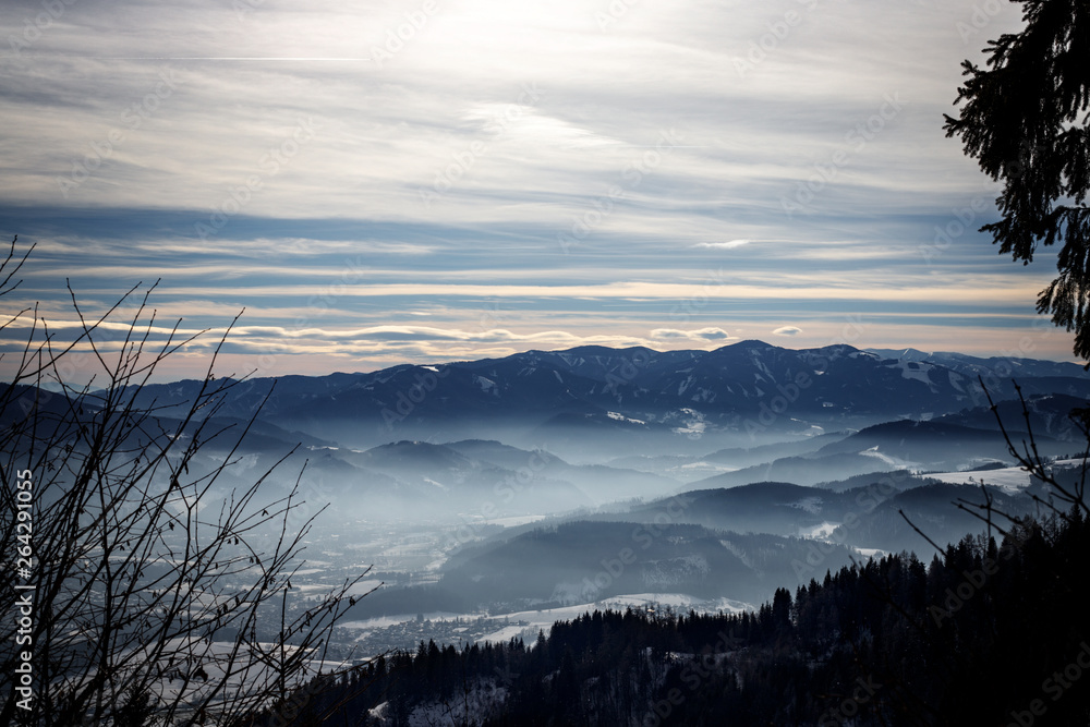 Alpine winter panorama with a misty valley with clouds and mountains foggy winter sky in the european alps