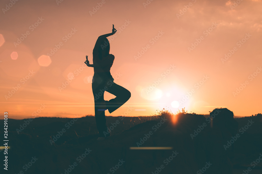 Silhouette di una ragazza in posizione di Yoga a una gamba su una montagna  di fronte all'alba arancione. Stock Photo | Adobe Stock