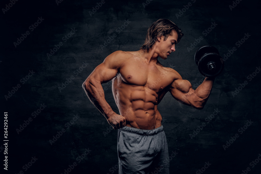 Attractive muscular man is posing with dumbbell. He has naked torso.