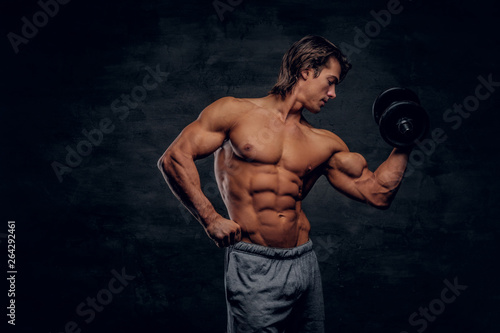 Attractive muscular man is posing with dumbbell. He has naked torso. © Fxquadro