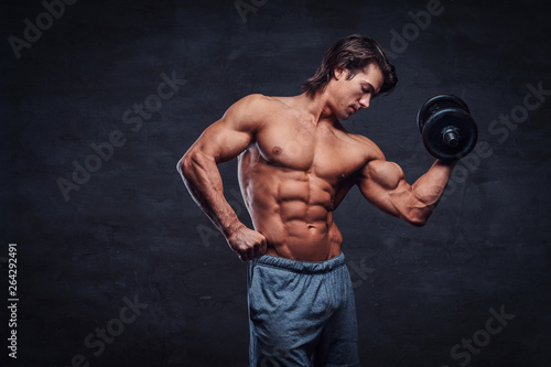 Attractive shirtless bodybuilder is doing exercise with dumbbell. There is dark background. © Fxquadro