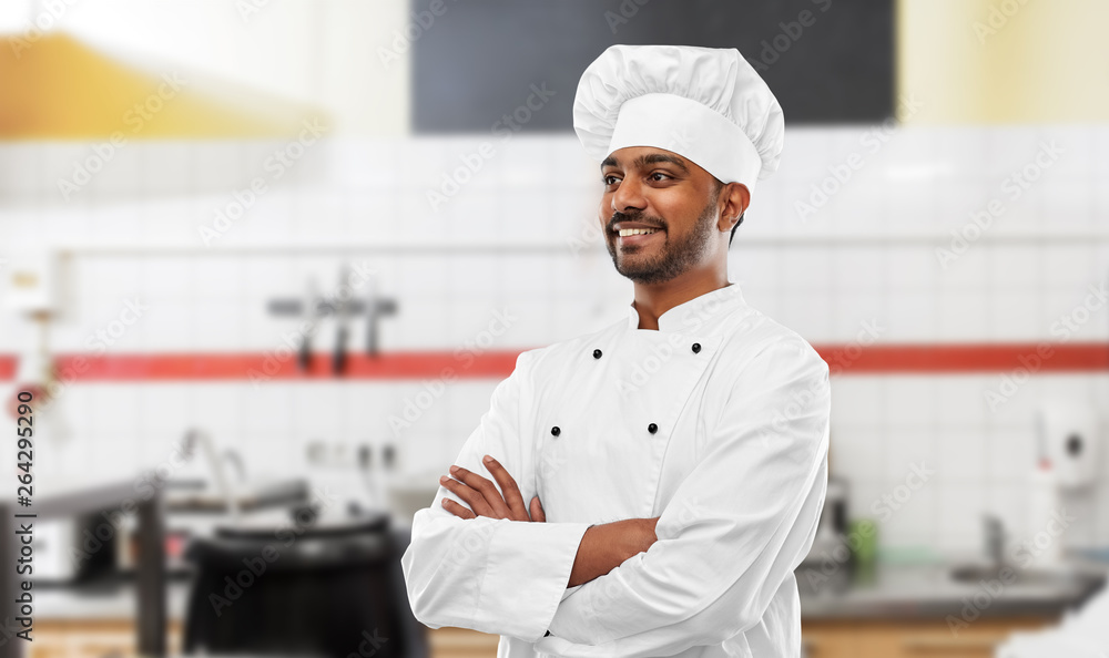 cooking, profession and people concept - happy male indian chef in toque over restaurant kitchen background