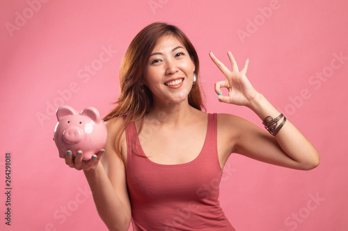 Asian woman show OK with pig coin bank.