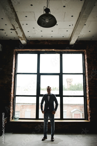 Silhouette of the guy in front of the window. Morning of the groom. Room in loft style. Big windows.