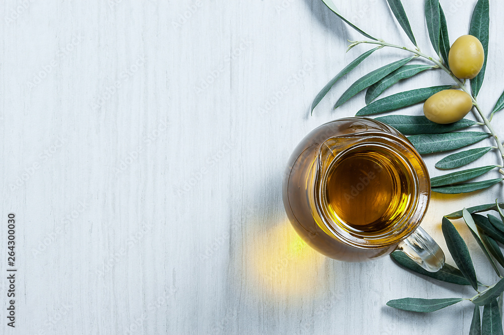 Glass bottle of homemade olive oil and olive tree branch, raw turkish green olive seeds and leaves on white table. olives background, olivae oleum Glass bottle of homemade olive oil and olive tree branch, raw turkish green olive seeds and leaves on white table. olives background, olivae oleum
