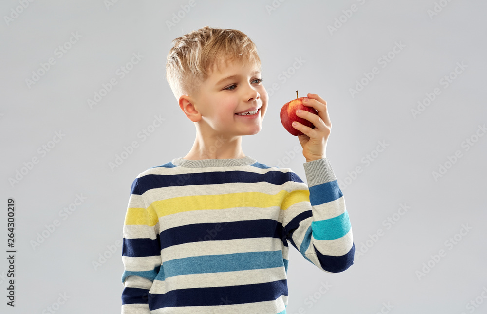 Naklejka premium food, diet and children concept - smiling boy in striped pullover eating red apple over grey background