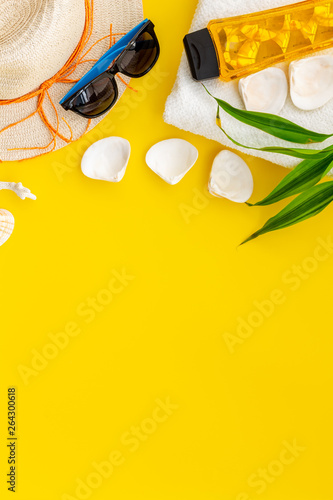 Summer travaling to the sea with straw hat, sun glasses, sunblock lotion on yellow background top view mock up