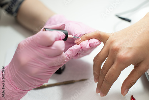 Closeup females hands getting manicure treatment from woman using small brush in salon environment  pink towel surface  blurry background products.