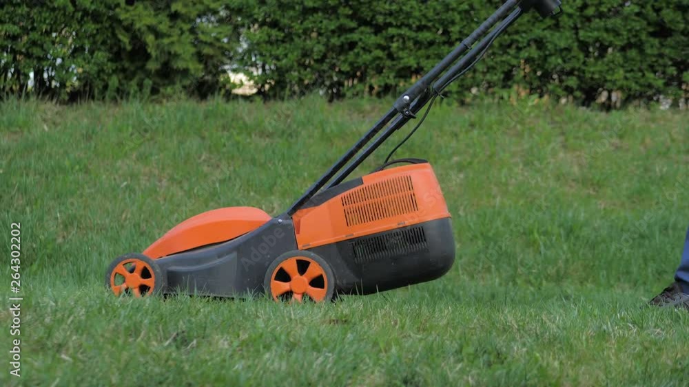 Adult man with electric lawnmower, lawn mowing. Gardener trimming a garden Adult man with electric lawnmower, lawn mowing. Gardener trimming a garden
