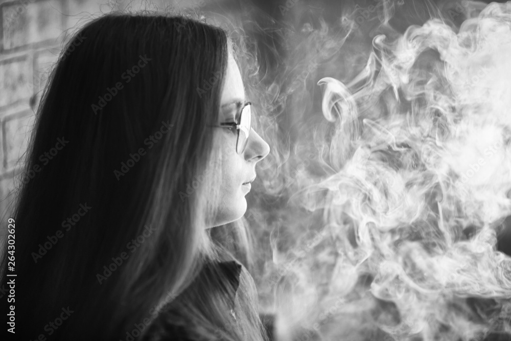 Vape teenager with  problem skin. Portrait of young cute girl in sunglasses smoking an electronic cigarette in the bar. Bad habit that is harmful to health. Vaping activity. Black nad white. Close up.