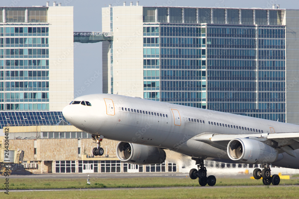 Close up of wide-body modern passenger airplane take off, building on background. Low over the runway. Vacation, aviation, trip concept Close up of wide-body modern passenger airplane take off, building on background. Low over the runway. Vacation, aviation, trip concept