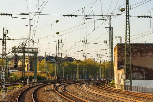 Outdoor diminishing perspective view of curve railway track lines without train and mess complex electric cables and poles with golden light atmosphere and evening before sunset sky.
