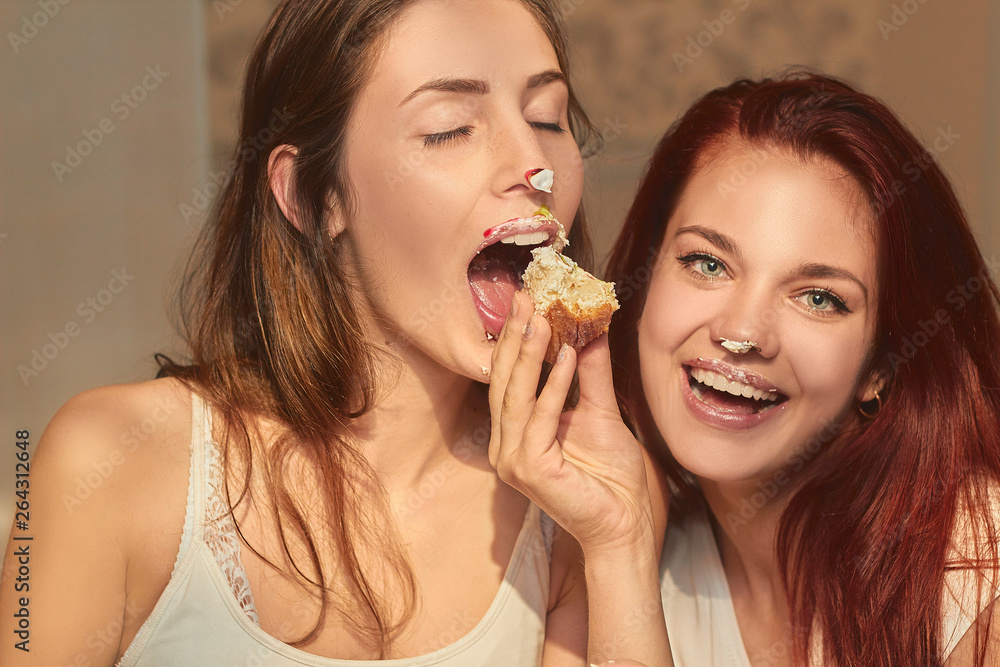Two beautiful ladies have birthday party. Best friends indulging, smearing cake on their faces. Sisters laughing and celebrating holiday. Friendship and food fetish concept. Two beautiful ladies have birthday party. Best friends indulging, smearing cake on their faces. Sisters laughing and celebrating holiday. Friendship and food fetish concept.
