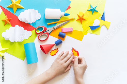 hands of the child make a paper craft rocket. Cosmos clouds and stars colored paper. The creative process
