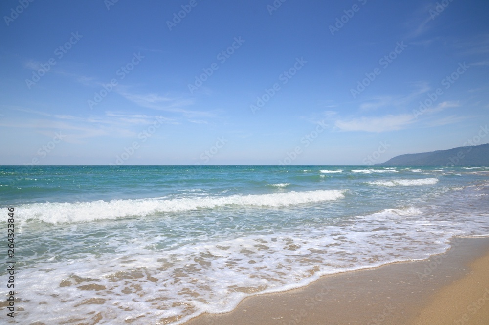 Turquoise tropical sea surf, wave foam, blue sky on empty sandy beach, Na Dan Beach in Khanom district of Nakhon Si Thammarat province of Thailand.