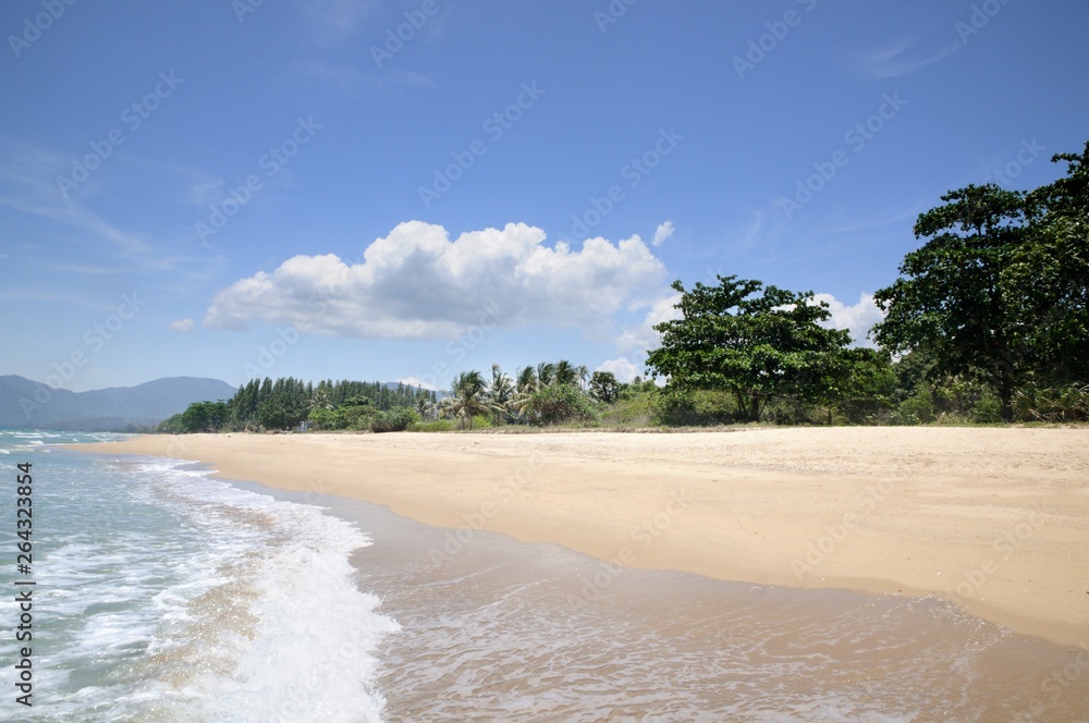 Obraz premium Turquoise tropical sea surf, wave foam, blue sky on empty sandy beach, Na Dan Beach in Khanom district of Nakhon Si Thammarat province of Thailand.